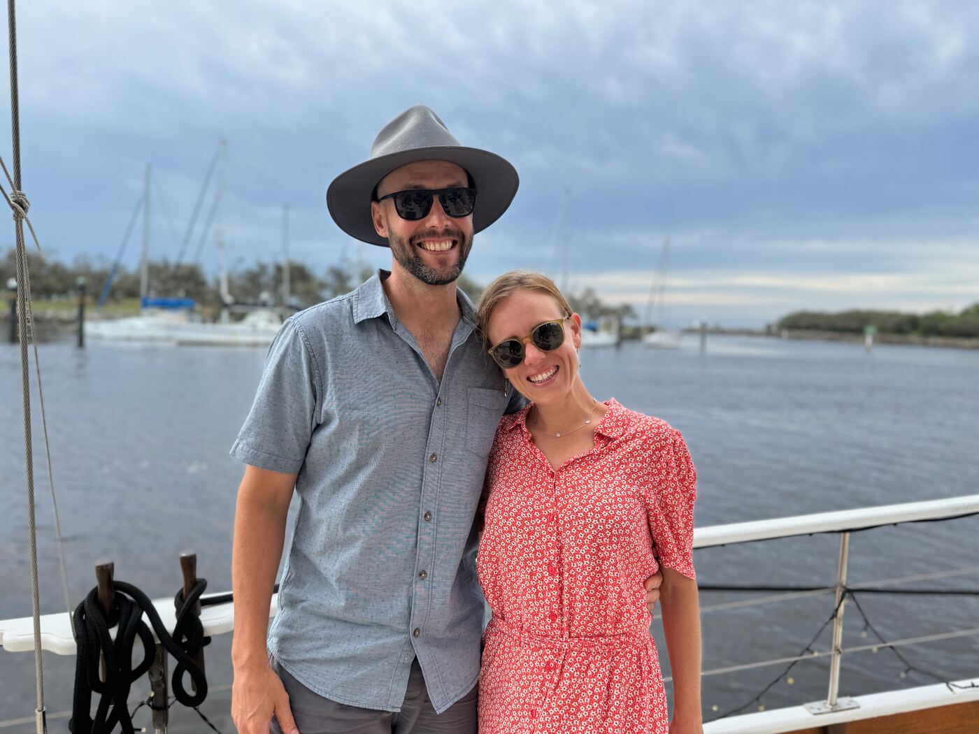 Jess and Greg on a boat deck in the evening, with the marina behind them.